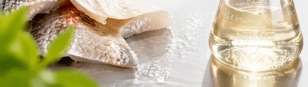 Raw fish skins on a steel bench beside a flask of clear collagen extract